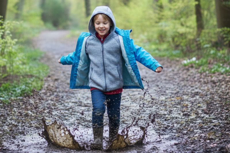 Chlapec v holánkách a pláštěnce skáče v lesní kaluži